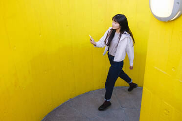 Junge Frau mit Mobiltelefon inmitten gelber Wände - ASGF02665