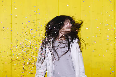 Carefree woman enjoying fallen confetti in front of wall - ASGF02669