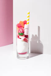 Glas mit Bündel von süßen Gummibonbons und weißen Zucker in der Nähe von gestreiften Strohhalm auf rosa und weißen Hintergrund platziert - ADSF36201