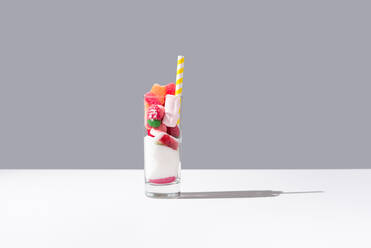 Glass with bunch of sweet gummy candies and white sugar placed near striped straw on grey and white background - ADSF36202
