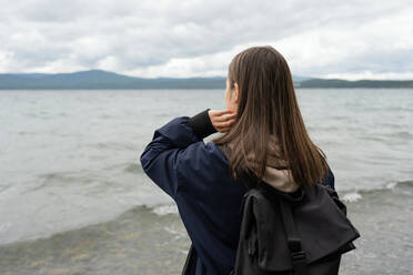 Rückenansicht eines anonymen Mädchens mit Regenmantel am Meeresufer - ADSF36205