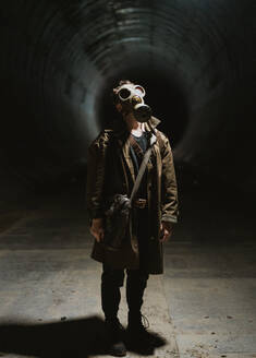 Ganzer Körper eines unkenntlichen männlichen Forschers mit Gasmaske in einem dunklen unterirdischen Tunnel während der Apokalypse - ADSF36210