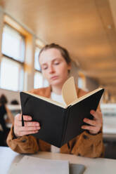 Weichzeichner einer jungen Frau, die am Tisch sitzend in einer Universitätsbibliothek ihre Notizen im Planer überprüft - ADSF36230