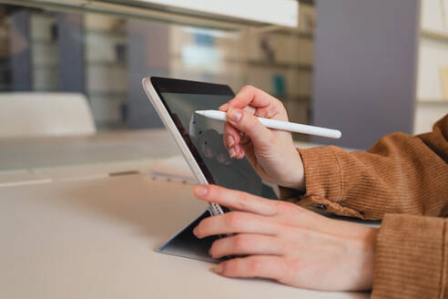 Unbekannte Frau mit Stift, die sich Notizen auf einem Tablet macht, während sie in einer Bibliothek tagsüber Hausaufgaben macht - ADSF36235