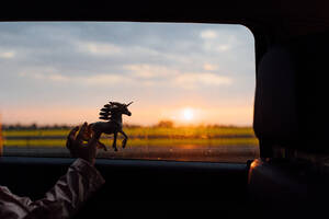 Crop anonyme Kind spielt mit Pferd Spielzeug in der Nähe von Fenster des Reitens Auto auf dem Lande bei Sonnenuntergang - ADSF36253