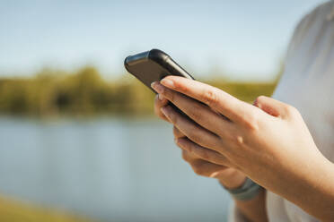 Frauenhand mit Mobiltelefon an einem sonnigen Tag - ACPF01447