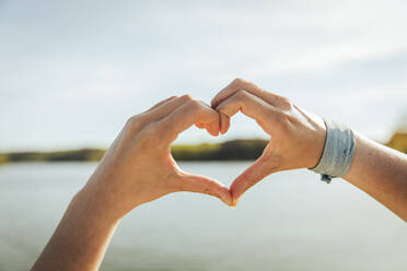 Young woman making heart shape on sunny day - ACPF01449