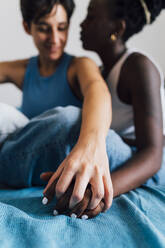 Lesbisches Paar hält sich an den Händen und sitzt auf dem Bett - MEUF07878