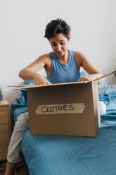 Young woman packing donation box in bedroom - MEUF07894