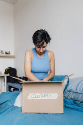 Young woman packing box for clothes donation on bed at home - MEUF07897