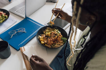 Businesswoman eating poke sitting with tablet PC at home - MEUF07916