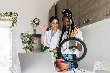 Smiling woman with friend filming plant care tutorial at home - MEUF07924