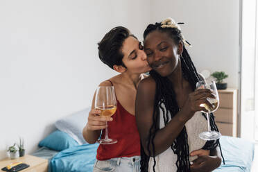 Frau hält Weinglas und küsst Freundin zu Hause - MEUF07942