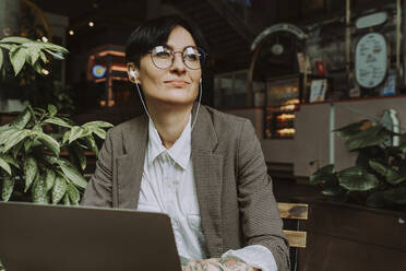 Lächelnde Geschäftsfrau mit Brille hört Musik über Kopfhörer - OIPF02296