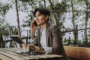 Geschäftsfrau mit kurzen Haaren, die in einem Straßencafé mit ihrem Smartphone telefoniert - OIPF02303