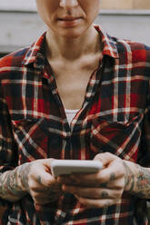 Woman with tattoo text messaging through smart phone - OIPF02309