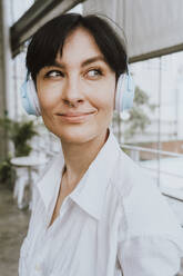 Lächelnde Geschäftsfrau mit kurzen Haaren hört Musik über drahtlose Kopfhörer - OIPF02318