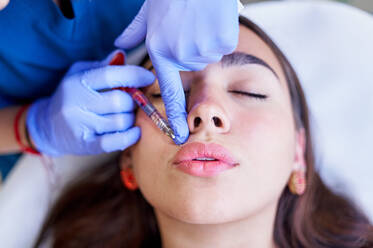 Von oben Ernte unerkennbar Kosmetikerin in Latexhandschuhen Injektion von Kollagen in die Lippen von entspannten weiblichen Kunden während der Sitzung in Schönheitsklinik - ADSF36269