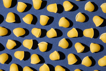 Draufsicht auf ungekochte Nudeln, die auf blauem Hintergrund angeordnet sind und ein nahtloses Muster bilden - ADSF36273
