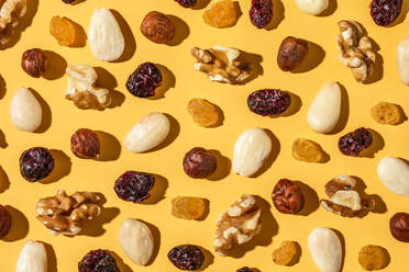 Top view assorted nuts and sweet raisins forming seamless pattern on yellow background - ADSF36274