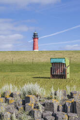 Germany, Schleswig-Holstein, Pellworm, Hooded beach chair with rock formation in foreground and Pellworm Lighthouse in background - KEBF02398