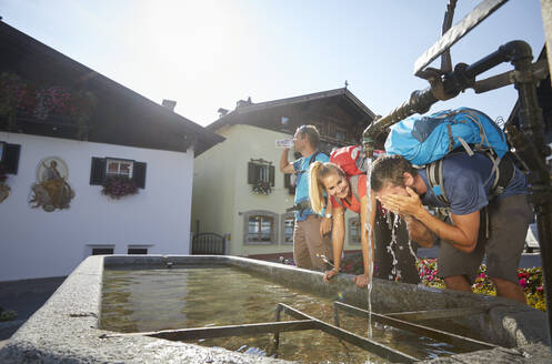 Wanderer wäscht sich das Gesicht mit Freunden am Brunnen im Dorf an einem sonnigen Tag, Mutters, Tirol, Österreich - CVF02173