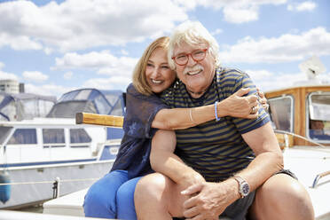 Frau umarmt älteren Mann, der auf dem Bootsdeck sitzt - RHF02613