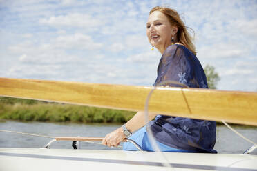 Smiling senior woman enjoying vacation sitting on deck - RHF02615