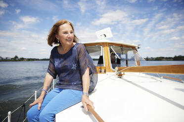 Happy senior woman sitting on boat deck at vacation - RHF02621