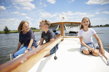 Siblings with grandmother sitting on boat deck at vacation - RHF02624