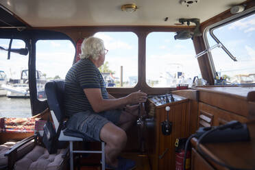Älterer Mann, der im Urlaub im Cockpit eines Segelboots sitzt - RHF02633