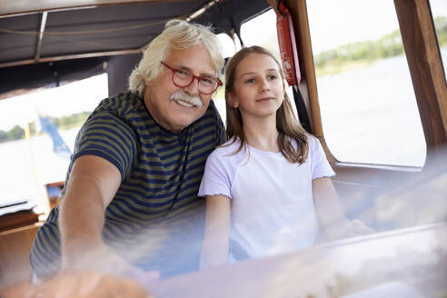 Lächelnder älterer Mann mit Enkelin auf einem Segelboot - RHF02638