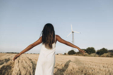 Woman with arms outstretched standing on wheat field in front of sky - SIF00348