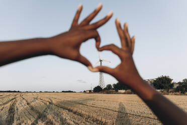 Frau macht Herzform mit Händen vor dem Himmel auf dem Bauernhof - SIF00359