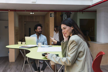 Lächelnde Geschäftsfrau sitzt am Tisch im Büro - PNAF04361