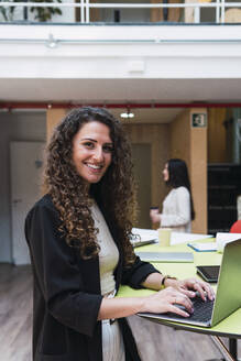 Porträt einer lächelnden brünetten Geschäftsfrau mit Laptop im Büro - PNAF04376