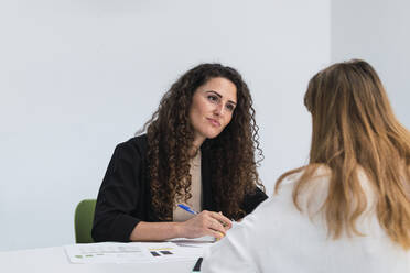 Businesswoman at desk looking at woman in office - PNAF04435