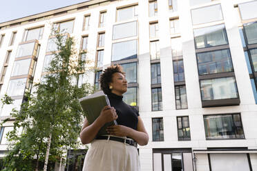Businesswoman with laptop in front of office building - VPIF06946
