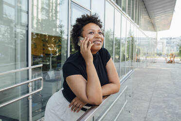 Lächelnde Geschäftsfrau, die mit ihrem Handy telefoniert und sich auf ein Geländer stützt - VPIF06955