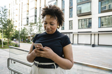 Happy businesswoman using smart phone in front of railing - VPIF06957