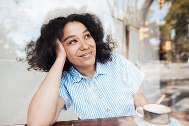 Lächelnde Frau mit Kaffeetasse sitzt am Tisch in einem Café - JOSEF11859