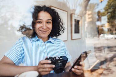 Lächelnde Frau mit Kamera und Mobiltelefon in einem Cafe - JOSEF11922