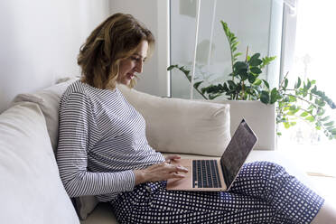 Frau sitzt auf dem Sofa und benutzt einen Laptop im heimischen Wohnzimmer - RFTF00266