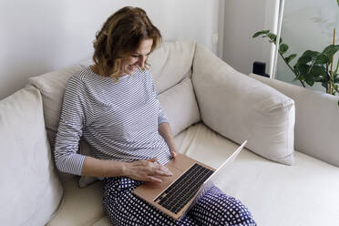 Lächelnde Frau benutzt Laptop zu Hause - RFTF00269