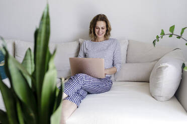 Lächelnde Frau mit Laptop auf der Couch zu Hause - RFTF00272