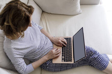 Reife Frau mit Laptop im Wohnzimmer sitzend zu Hause - RFTF00273