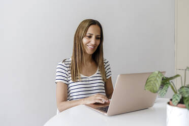 Smiling freelancer working on laptop sitting at home office - RFTF00286