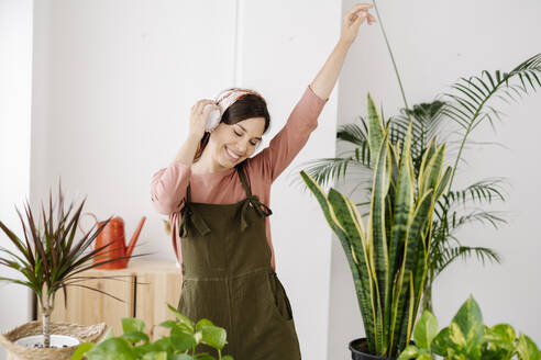 Lächelnde Frau hört Musik über Kopfhörer und tanzt inmitten von Pflanzen - JCZF01039