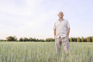Ein älterer Landwirt steht mit den Händen in den Taschen auf einem Bauernhof - EYAF02043