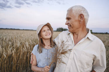 Lächelndes Mädchen hält Feldfrüchte und sieht Großvater auf dem Feld an - EYAF02064